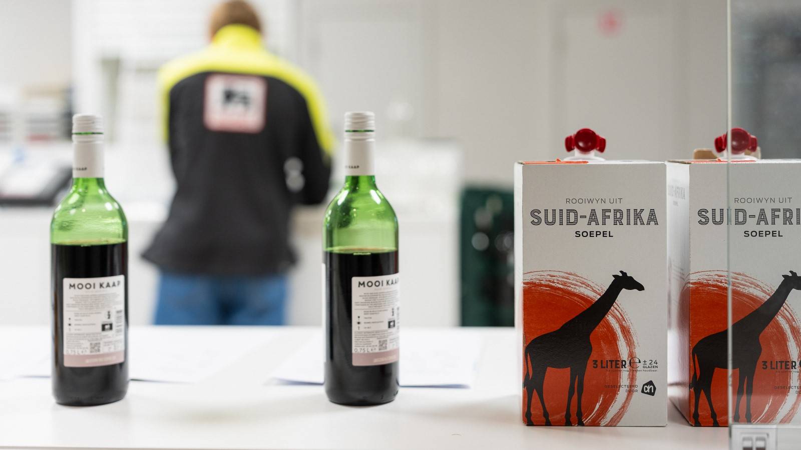 Wine bottles and carton wine packaging displayed side by side on a table in a packaging facility.