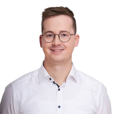 Portrait eines junger blonden Mannes mit Brille, mit weißem Hemd. Er lächelt in die Kamera.