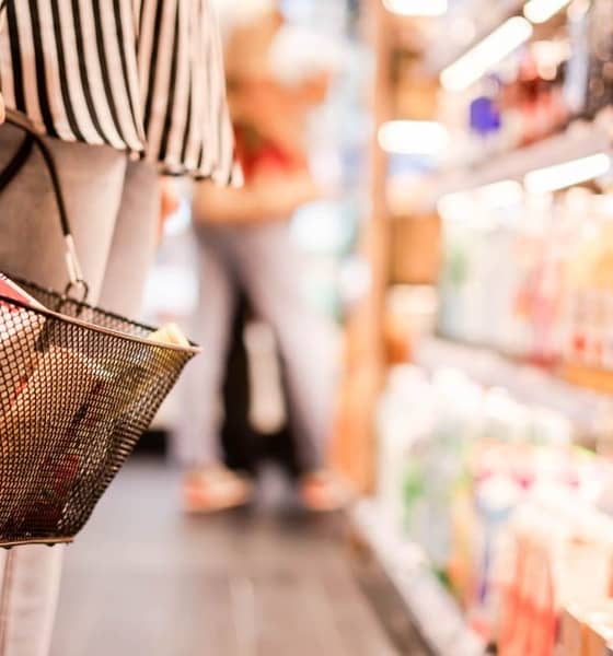 Eine Person steht mit einem gefülltem Einkaufskorb im Supermarkt.
