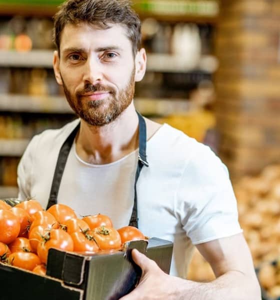 Mann im Supermarkt hält ein Tray gefüllt mit Tomaten in den Händen.