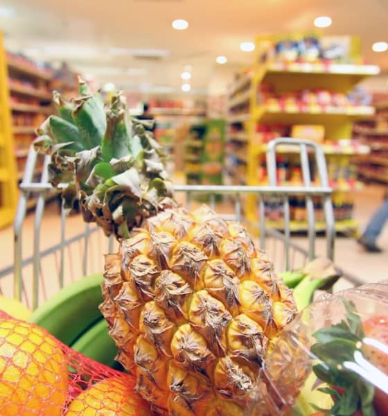 Eine Ananas im vollen Einkaufswagen ist fokussiert, während im Hintergrund ein Supermarkt zu sehen ist. 