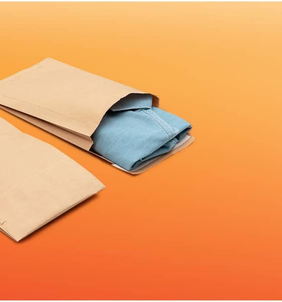 Zwei braune Papier Versandtaschen liegen auf orangenem Hintergrund nebeneinander. Eine ist geöffnet und ein Jeans Kleidungsstück schaut heraus.