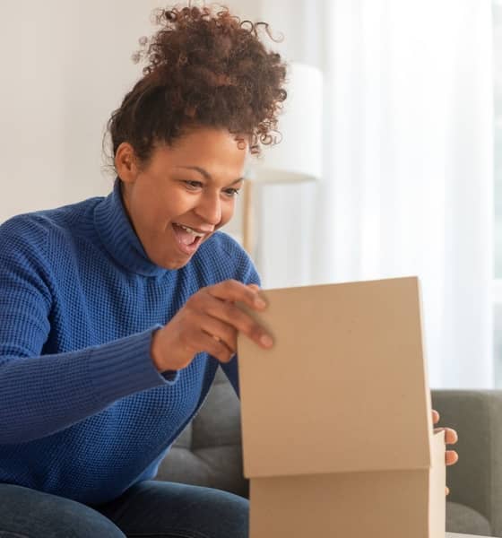 Eine Frau sitzt auf dem Sofa und freut sich, während sie ein Paket öffnet.