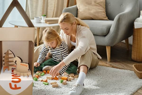 Mutter und Tochter spielen mit Bauklötzen auf dem Boden neben Wellpappverpackung