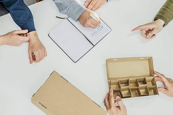 aaltopahvipakkaus keskellä ja käsiä ympärillä 