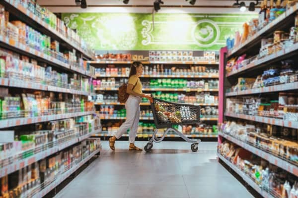 Frau im Supermarkt schiebt gefüllten Einkaufskorb