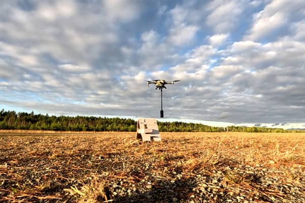 drone kuljettaa aaltopahvista jalustaa ja raivauspanoslaatikkoa pellolla