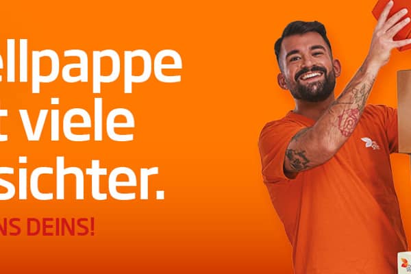 asiatische Frau mit langen Haaren steht seitlich eines Kartonstapels aus Wellpappe vor orangefarbenem Hintergrund und lächelt in die Kamera. Sie trägt ein orangefarbenes T-Shirt was deutlich Arbeitskleidung der Produktion ist.