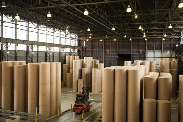 a forklift truck driving through giant reels of paper ina warehouse