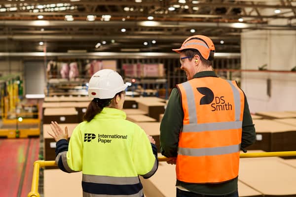 Two packaging plant workers, a man and a woman, seen from behind as they look over the plant. They are wearing reflective safety vests branded International Paper and DS Smith.