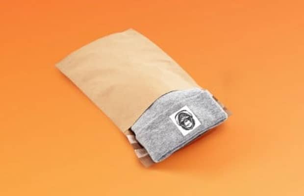Braune Versandtasche aus Papier mit Spitzboden gefüllt mit einer grauen Mütze.