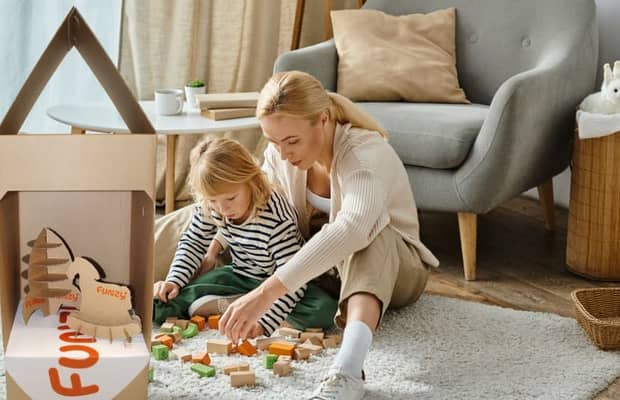 Mutter und Tochter spielen mit Bauklötzen auf dem Boden nebenWellpappverpackung