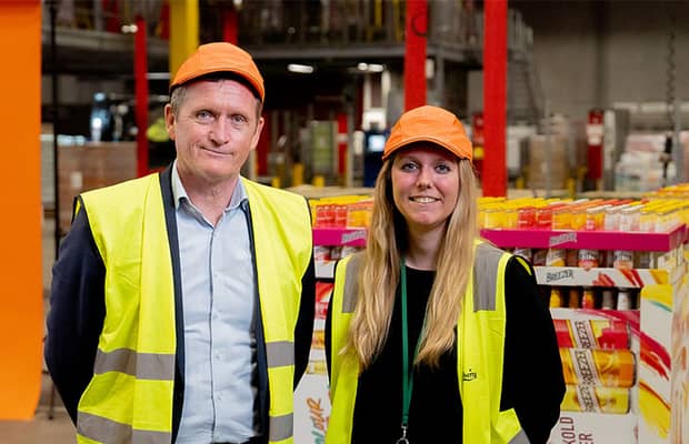 kaksi ihmistä seisoo automaatiolinjojen vieressä ja katsoo kameraan