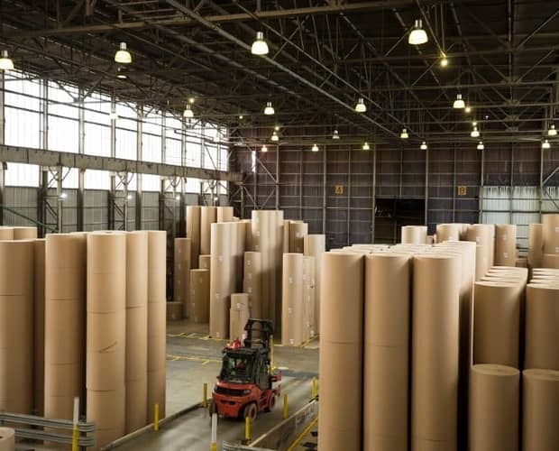 a forklift truck driving through giant reels of paper ina warehouse