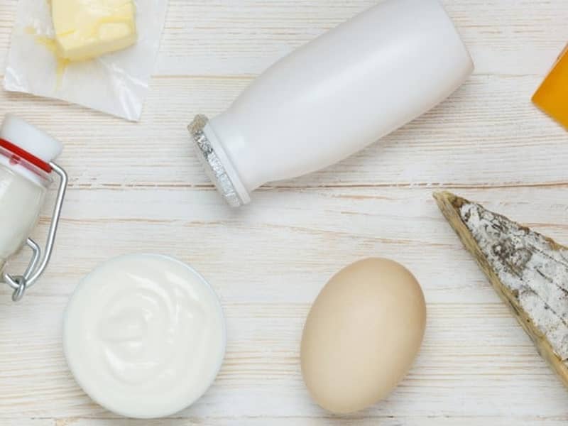 Auf einem Tisch stehen ein Ei, Milch, Käse und eine Schale Joghurt.