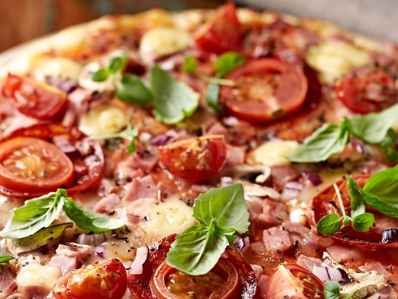 Nahaufnahme einer Pizza belegt mit Tomaten, Fleisch und Kräutern.