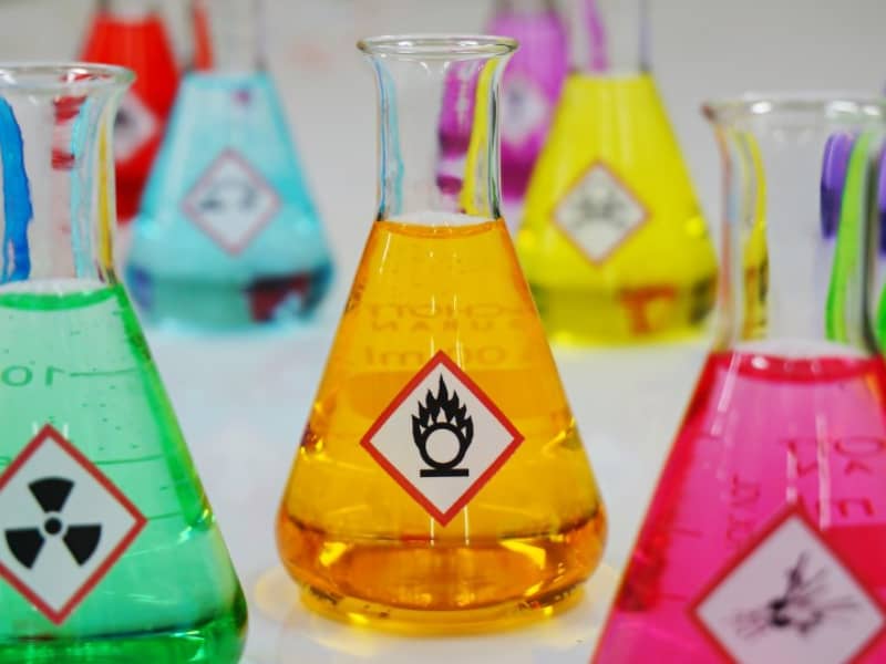 Mehrere Laborgläser mit Warnetiketten und gefüllt mit bunten Flüssigkeiten.