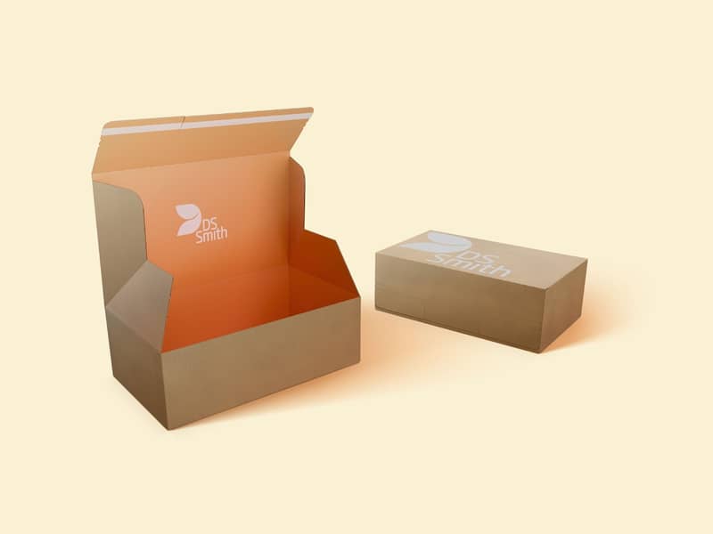 Einge geschlossene braune Verpackung mit weißem DS Smith Logo liegt hinter einer offener einteiliger brauner Verpackung mit orangem Innendruck und DS Smith Logo.