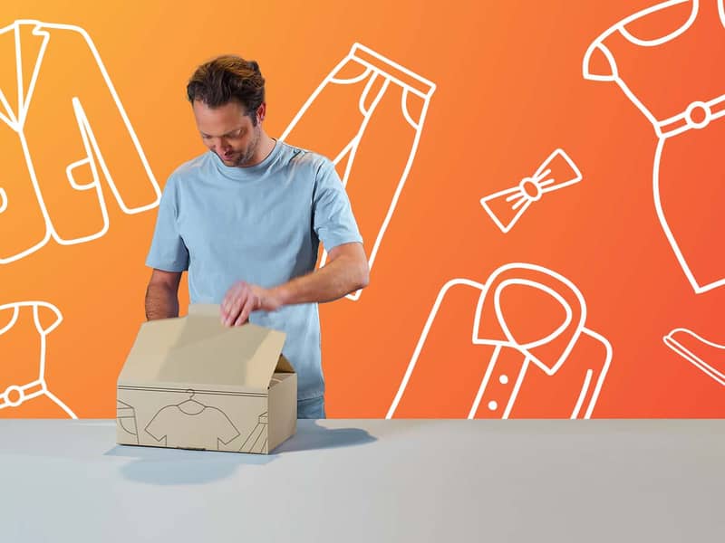 Ein Mann öffnet eine braune Verpackung welche mit Kleidungsstücken bedruckt ist. Der Hintergrund ist orange und es sind weiße Umrisse unterschiedlicher Kleidungsstücke darauf zu sehen.