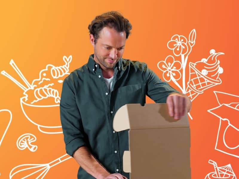 Ein Mann öffnet eine braune Verpackung. Der Hintergrund ist orange mit Umrissen von unterschiedlichen Gegenständen zum Thema Essen.