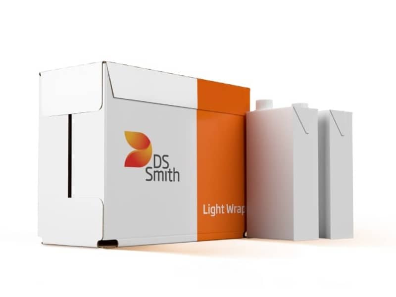 Umverpackung aus Wellpappe für Getränke neben zwei weißen Getränkekartons.