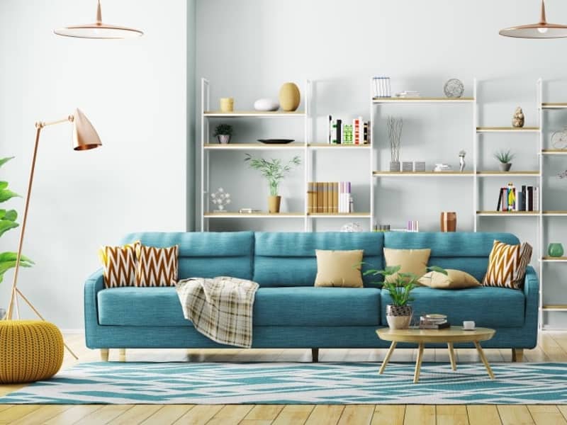 Frontansicht in ein Wohnzimmer mit blauem Sofa vorne und weißem Regal im Hintergrund.