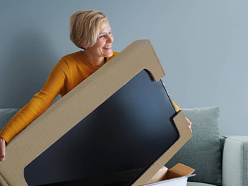 Vrouw op bank met televisie in kartonnen verpakking