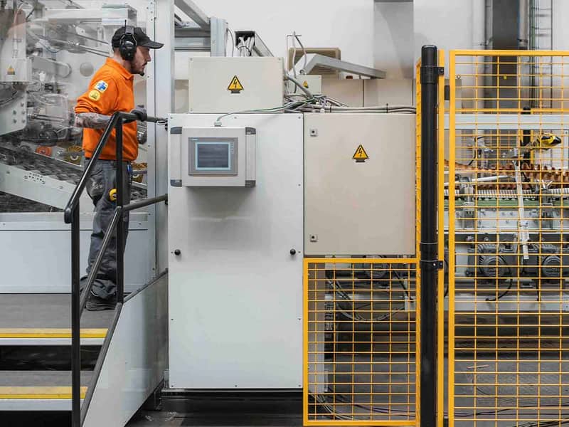 Een man staat op een trap voor een verwerkingsmachine voor golfkartonnen verpakkingen bij DS Smith in Harelbeke