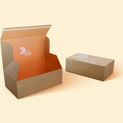 Einge geschlossene braune Verpackung mit weißem DS Smith Logo liegt hinter einer offener einteiliger brauner Verpackung mit orangem Innendruck und DS Smith Logo.