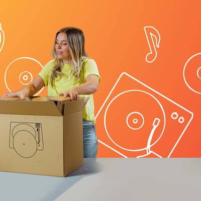 Eine blonde Frau hantiert mit einer auf einem Tisch stehenden Verpackung. Auf der braunen Verpackung ist ein Schallplattenspieler zu sehen und der Hintergrund ist orange mit verschiedenen Musikzeichnungen.