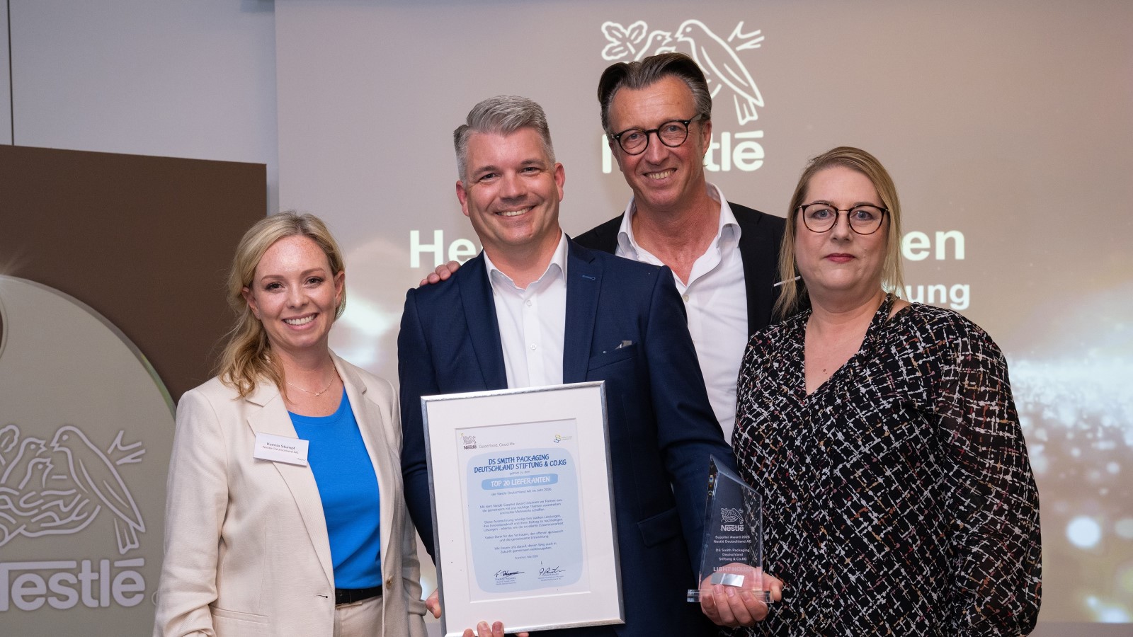 Four representatives at a Nestlé supplier award event holding an award trophy and recognition certificate.