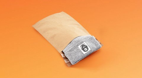 Braune Versandtasche aus Papier mit Spitzboden gefüllt mit einer grauen Mütze.