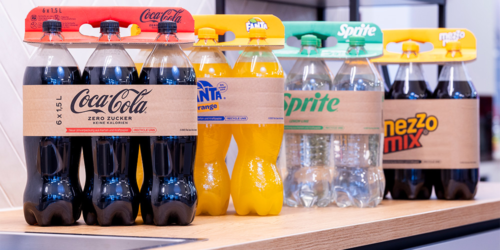 La imagen muestra la innovadora solución de embalaje de DS Smith: Lift Up. Hay cuatro paquetes de seis unidades uno detrás de otro, incluyendo Coca-Cola, Fanta, Sprite y Mezzo Mix. Cada paquete cuenta con un Lift Up.