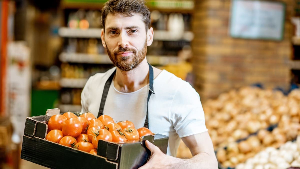 Mann im Supermarkt hält ein Tray gefüllt mit Tomaten in den Händen.
