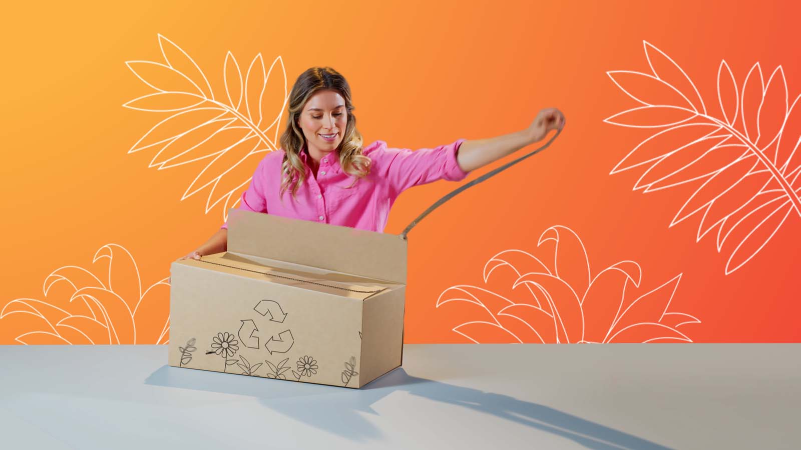 Eine blonde Frau öffnet eine braune Verpackung welche auf einem grauen Tisch steht. Die Verpackung ist mit Blumen und einem Recyclingsymbol bedruckt.