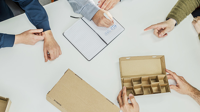 aaltopahvipakkaus keskellä ja käsiä ympärillä 