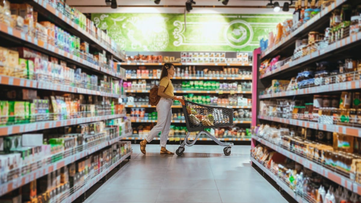 Frau im Supermarkt schiebt gefüllten Einkaufskorb