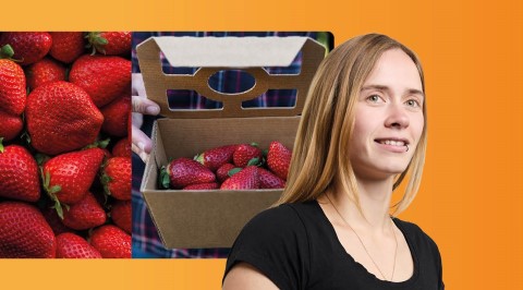 Frau im Vordergrund schaut nach vorne, während im Hintergrund Wellpappschalen mit Erdbeeren präsentiert sind.