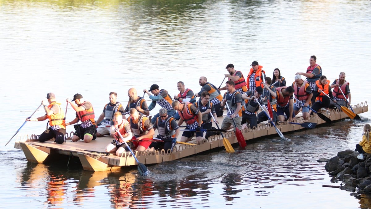 DS Smith Mitarbeitende paddeln mit dem Boot aus Wellpappe über das Wasser. 