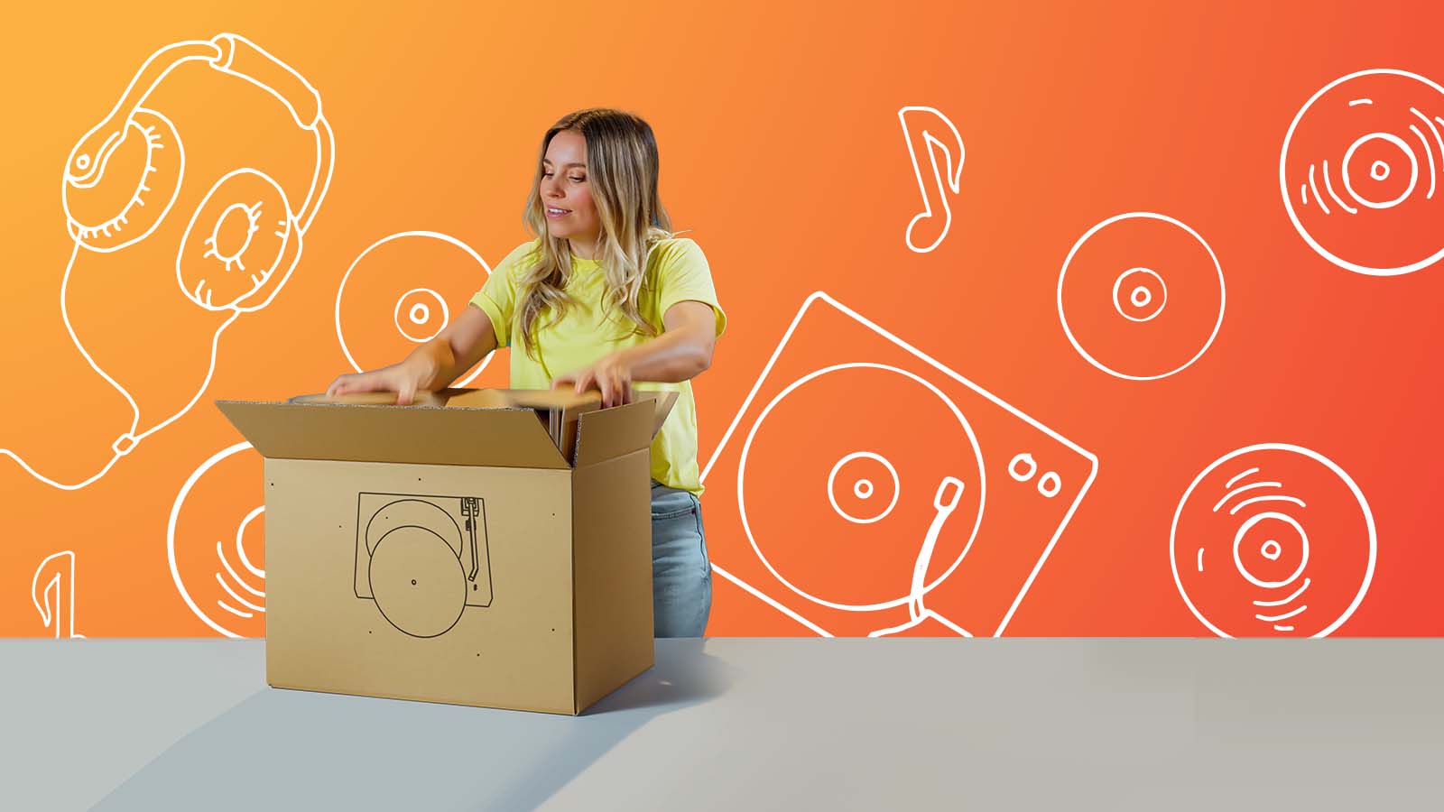 Frau öffnet eine Verpackung aus Wellpappe in welcher sich ein Plattenspieler befindet.