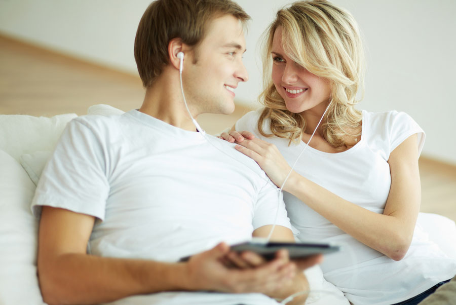 Man en vrouw luisteren op de bank lachend naar muziek op hun tablet of smartphone