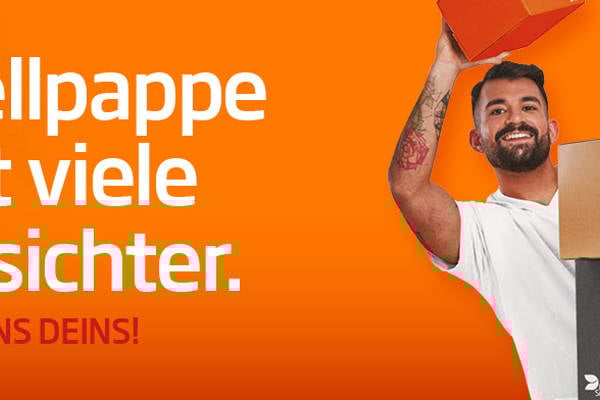 junger dunkelhaariger Mann mit weißem T-Shirt vor orangefarbenen Hintergrund lächelt in die Kamera und schaut an einem Kartonstapel aus Wellpappe vorbei einen hält kleinen Wellpappkarton in der Hand