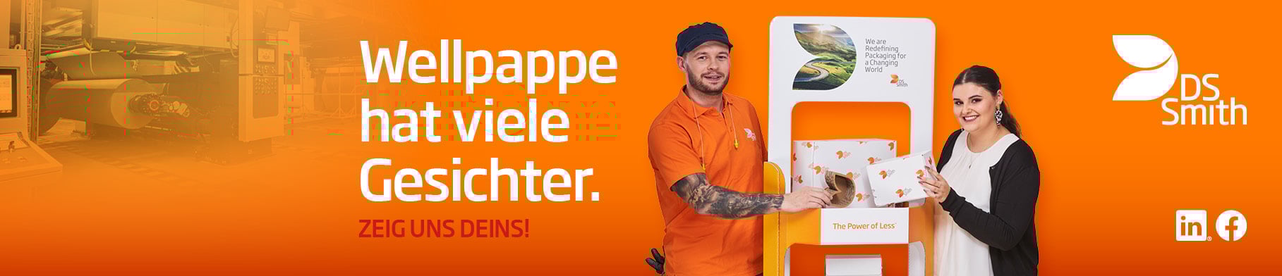 Links vom Aufsteller aus Wellpappe steht ein junger farbiger Mann mit schwarzen Haar in orangenem T-Shirt und lächelt in die Kamera. Rechts steht eine junge dunkelhaarige Frau mit weißer Bluse und dunkler Strickjacke und lächelt in die Kamera. Beide haben ein kleines Produkt aus Wellpappe in der Hand.