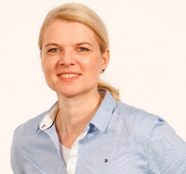  Portrait einer blonden Frau, zum Zopf gebundene Haare. Hellblaue Bluse. Sie lächelt in die Kamera.