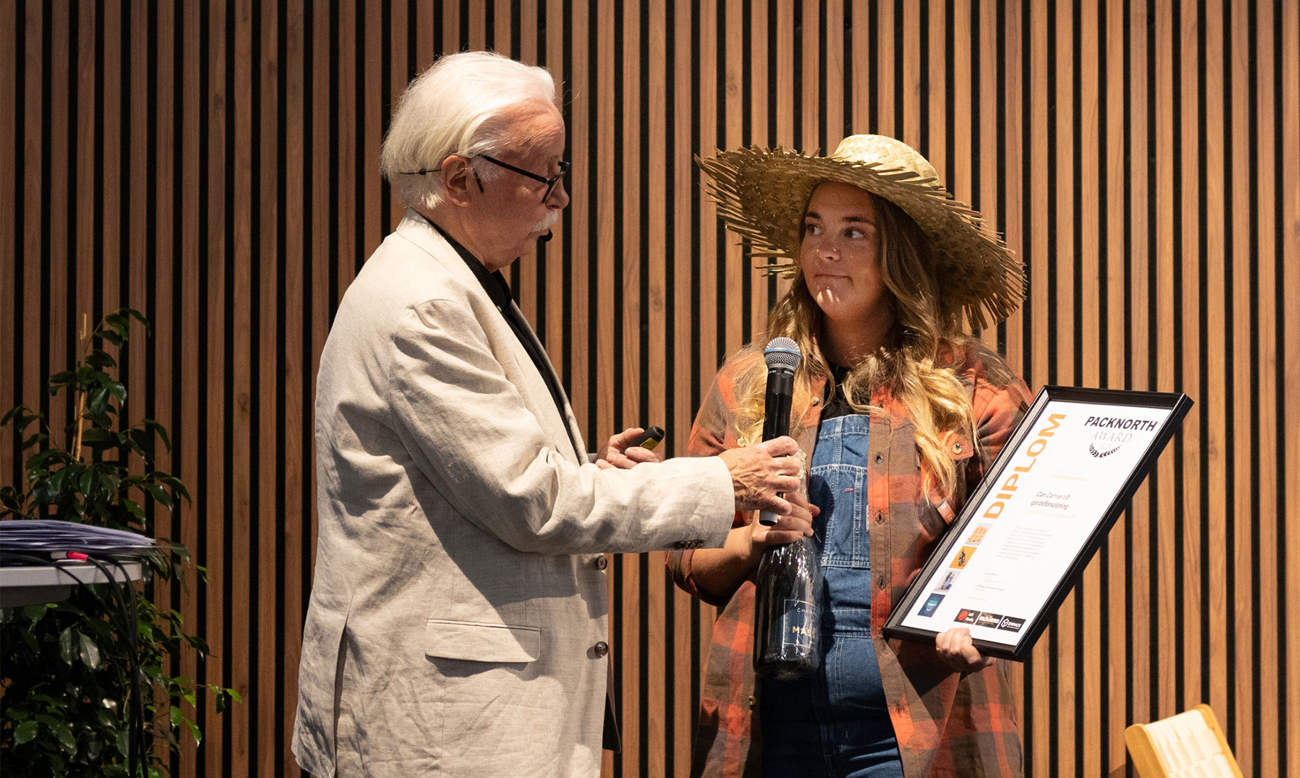 Emelie Karlsson från DS Smith tar emot Packnorth Award 2025 på scen. Hon håller diplom och champagneflaska medan prisutdelaren Bo Wallteg överlämnar mikrofonen under ceremonin.