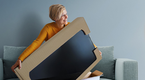 Vrouw op bank met televisie in kartonnen verpakking