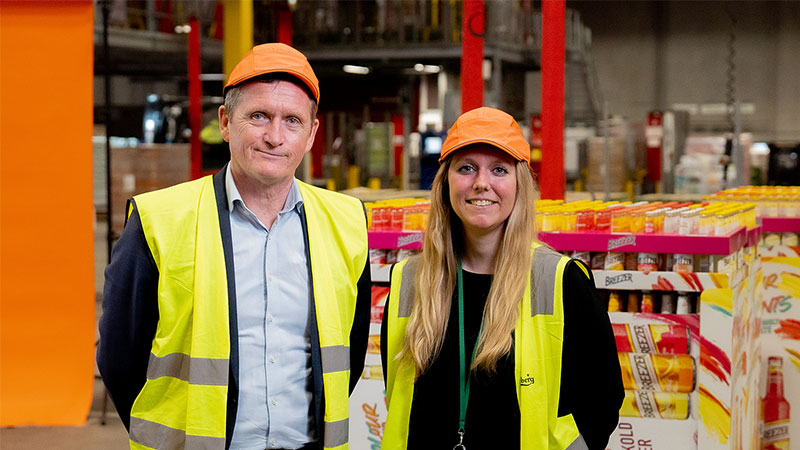 kaksi ihmistä seisoo automaatiolinjojen vieressä ja katsoo kameraan